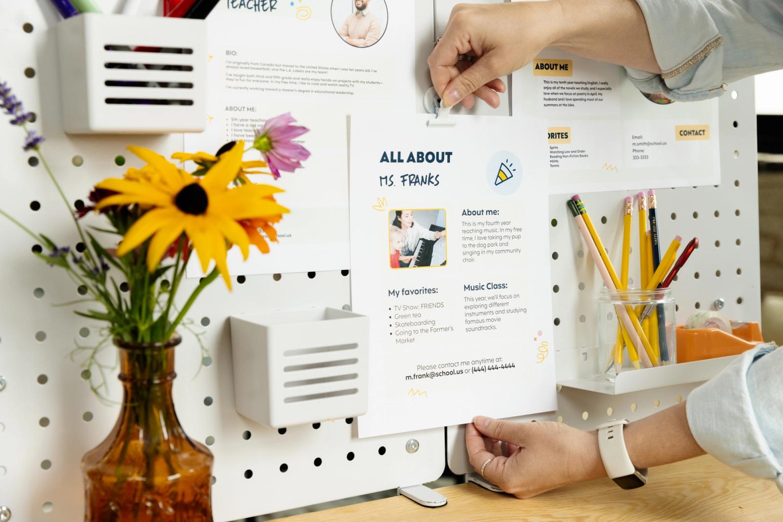 Hands reach in to place a poster on a white bulletin board. 