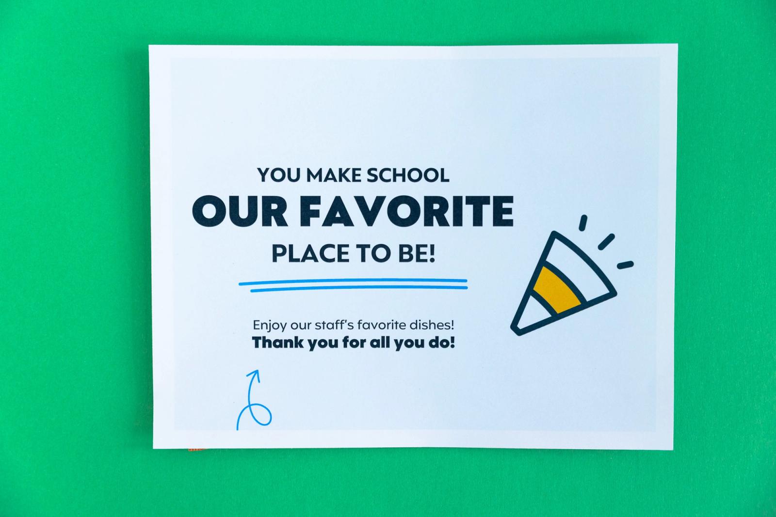 A sheet of paper that says "you make school our favorite place to be" lays on a green background.