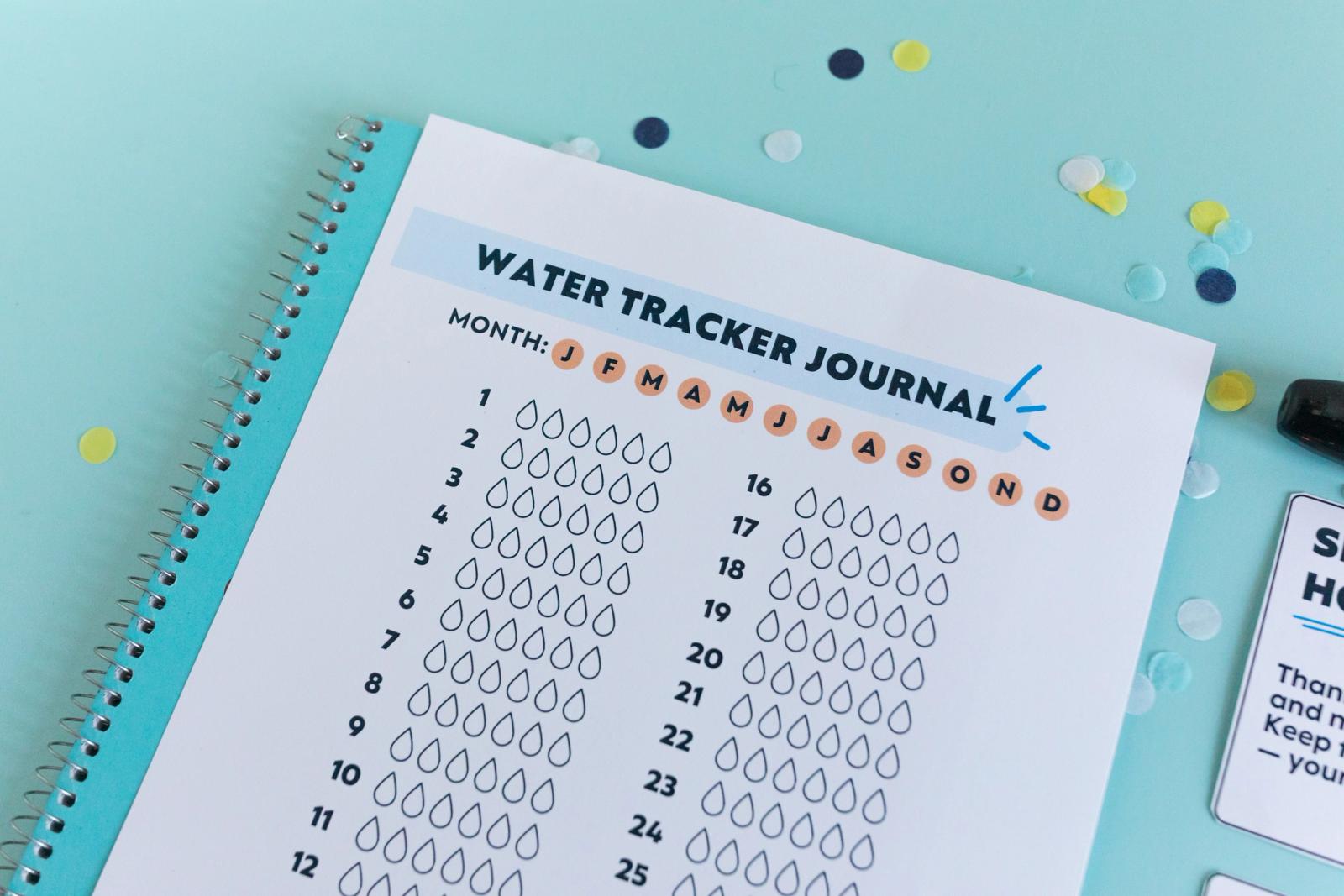 Close up of a piece of paper that says "water tracker journal" on a light blue background. 