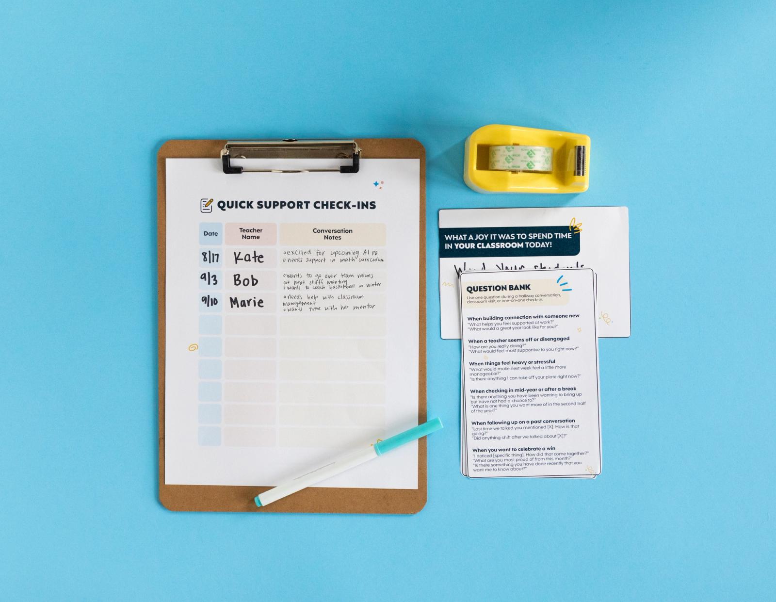 A sheet of paper with writing on it is on a clipboard with a blue marker on top sitting on a light blue background. A tape dispenser and notecards sit beside the clipboard.
