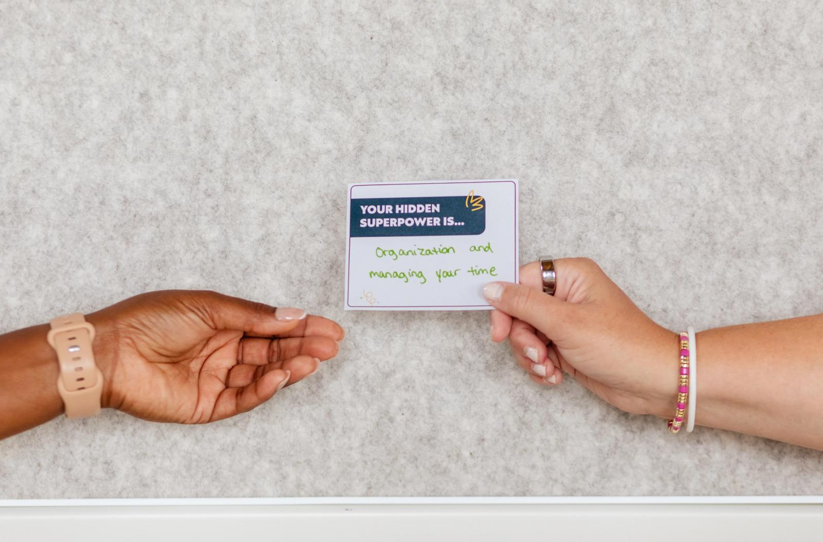 Two hands exchange a notecard with a handwritten note on it.
