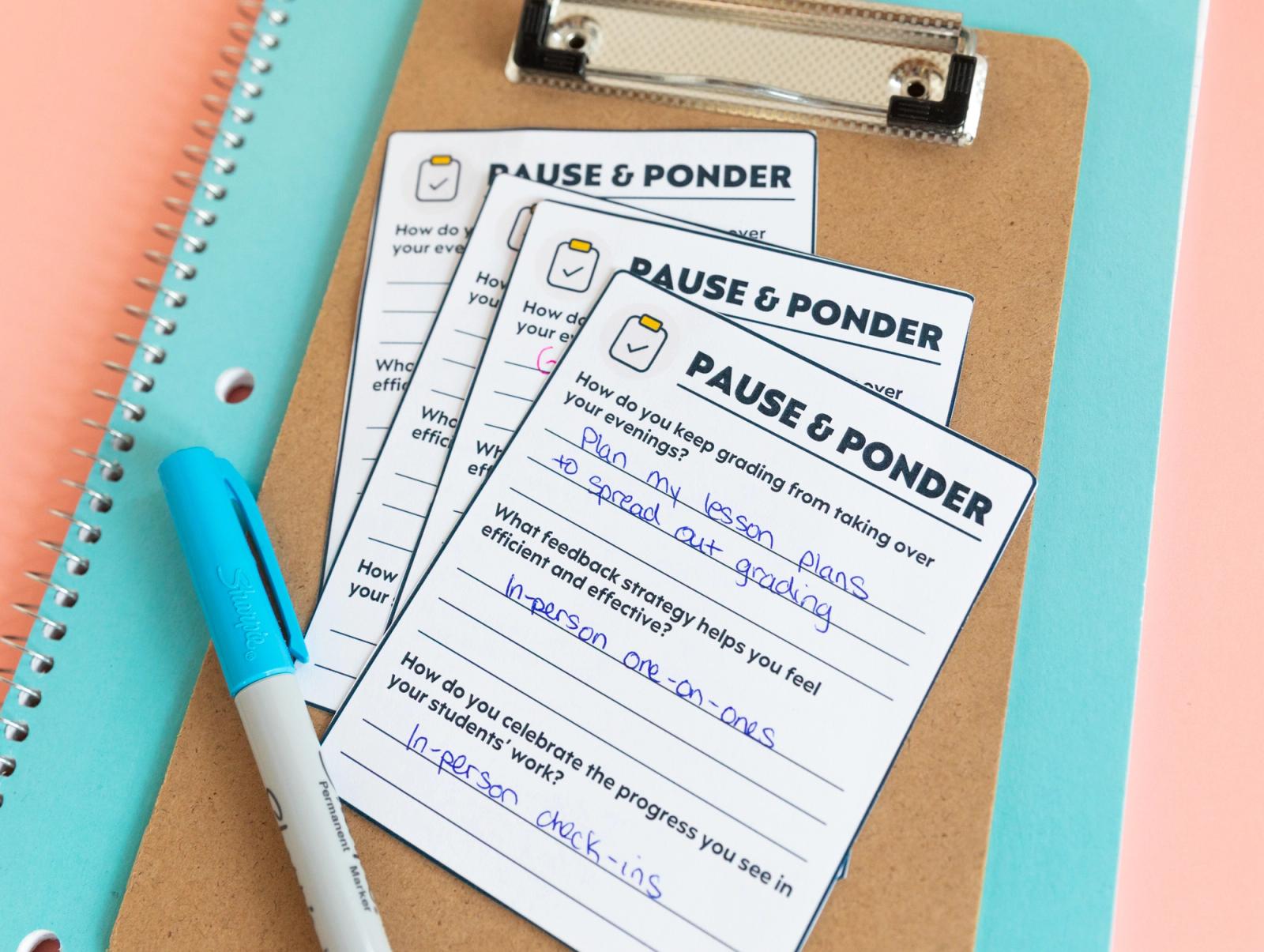 A blue notebook with a clipboard, notecards, and blue pen on it sits on a salmon background.