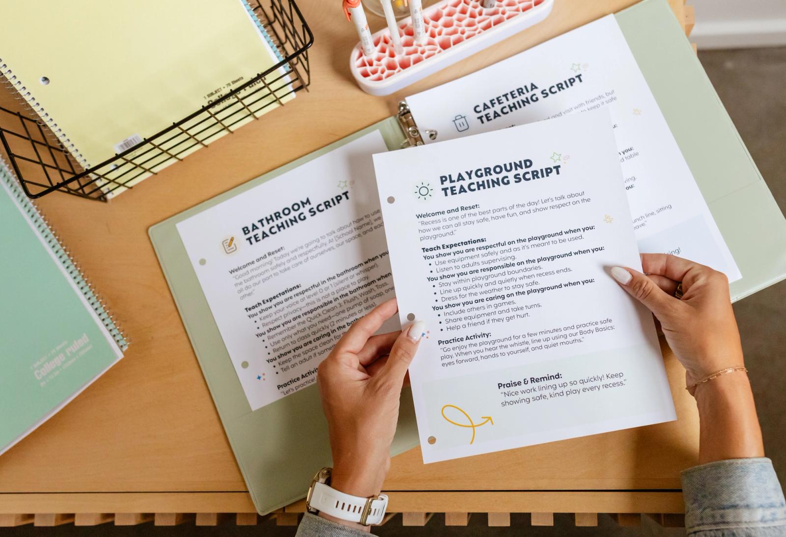 A binder full of papers lays open on a table. Two hands reach in and hold a piece of paper to place in the binder.