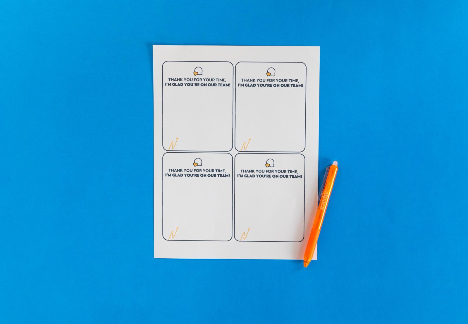 Sheet of paper with four notecards on it and an orange pen lay on a blue background