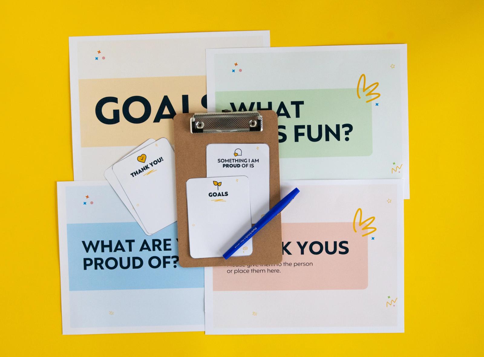 Four posters lay on a yellow background. On top of them are notecards, a clipboard, and blue marker.