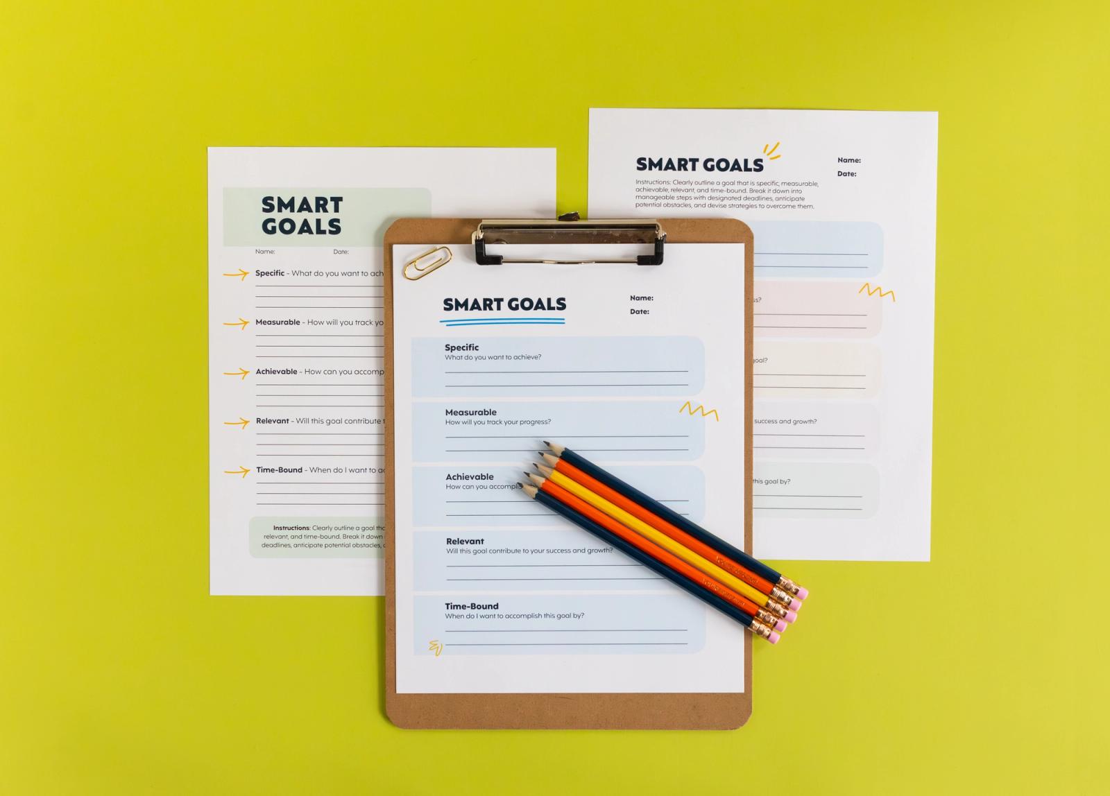 Two sheets of paper lay on a bright green background. A clipboard with a sheet of paper on it and pencils lay on top of the two sheets.