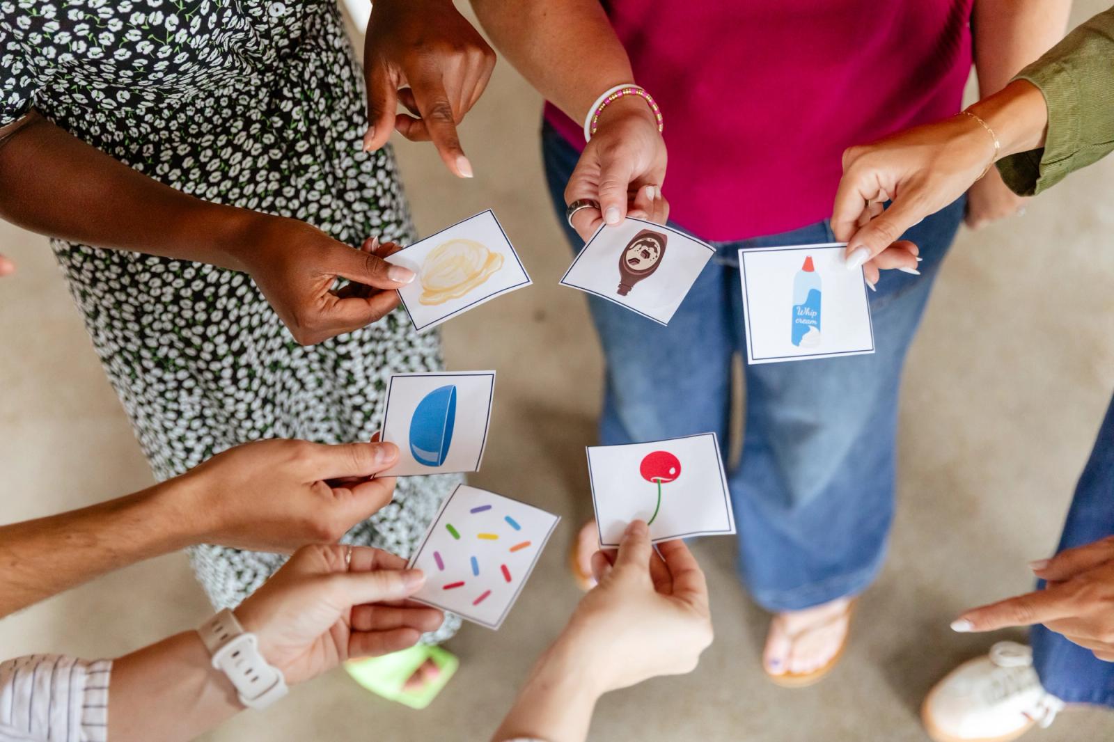 Hands reach into a circle, each one holds a small piece of paper with an image on it.