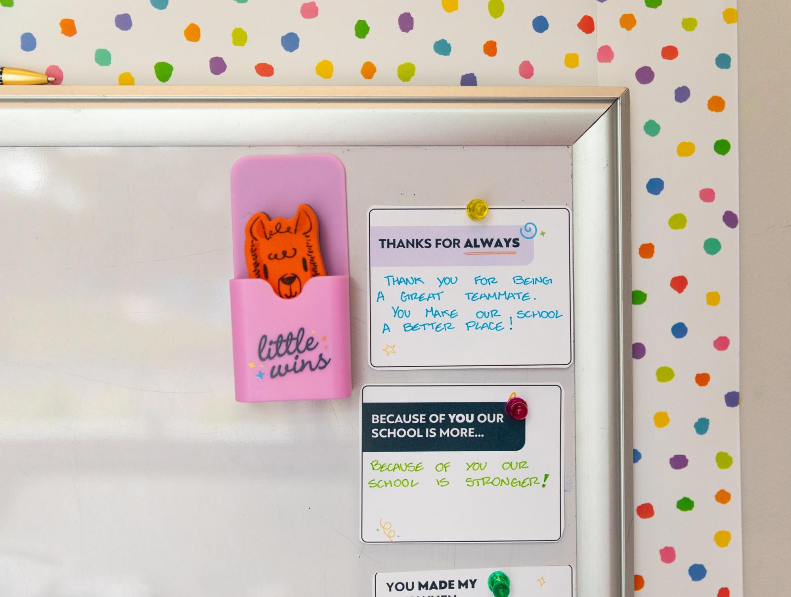Several handwritten notes are placed on a while bulletin board. Beside them is a whiteboard eraser in the shape of an alpaca in a holder that says "little wins."