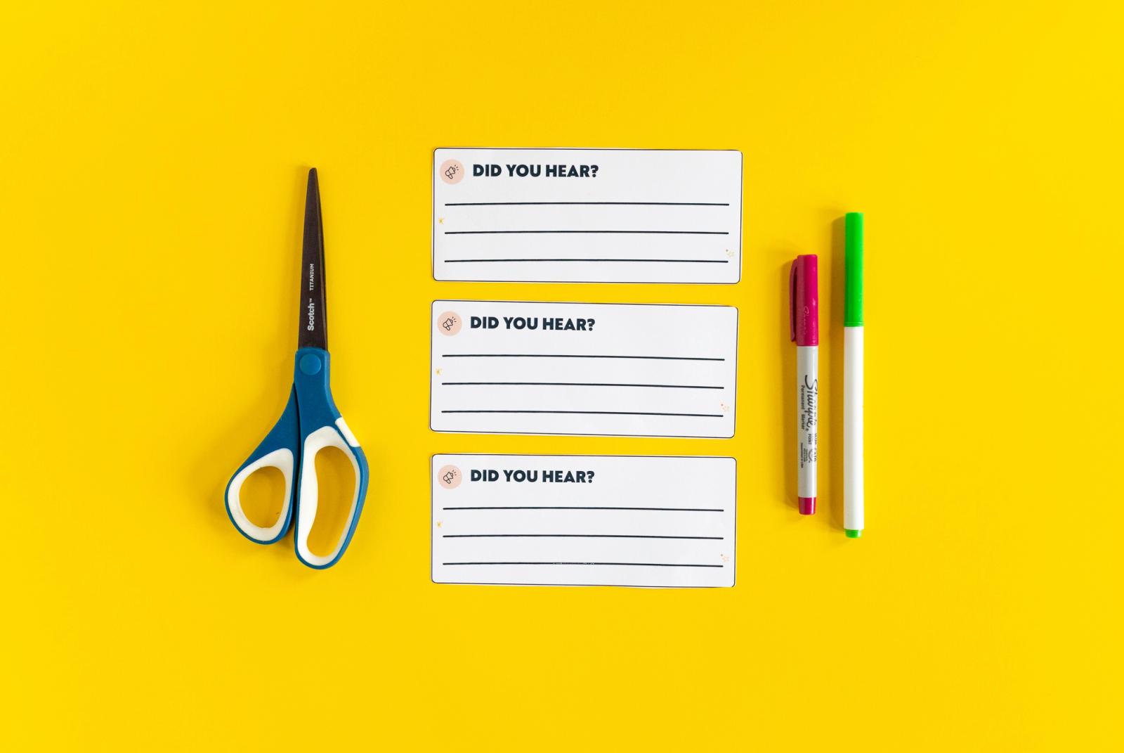 Three notecards that say "did you hear" lay on a yellow background. To the left is a pair of scissors, to the right is a red pen and green marker.