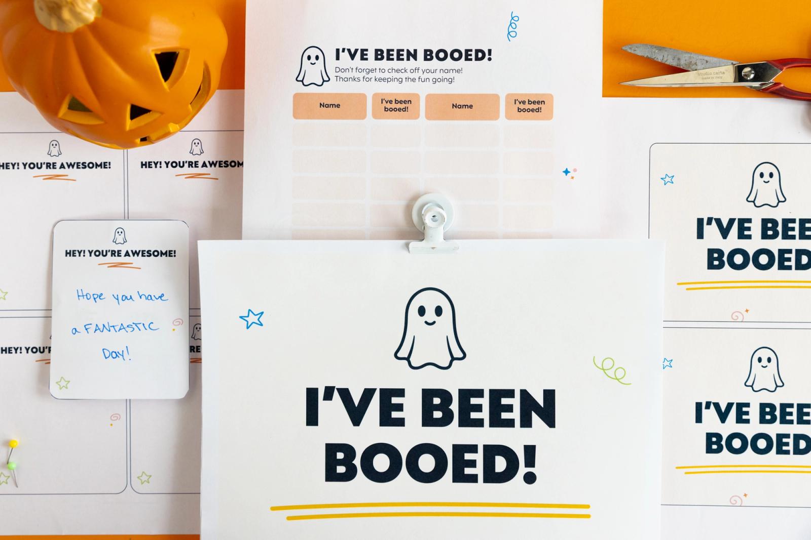 Several pieces of paper lay on an orange background. A pumpkin and pair of scissors lays next to them.