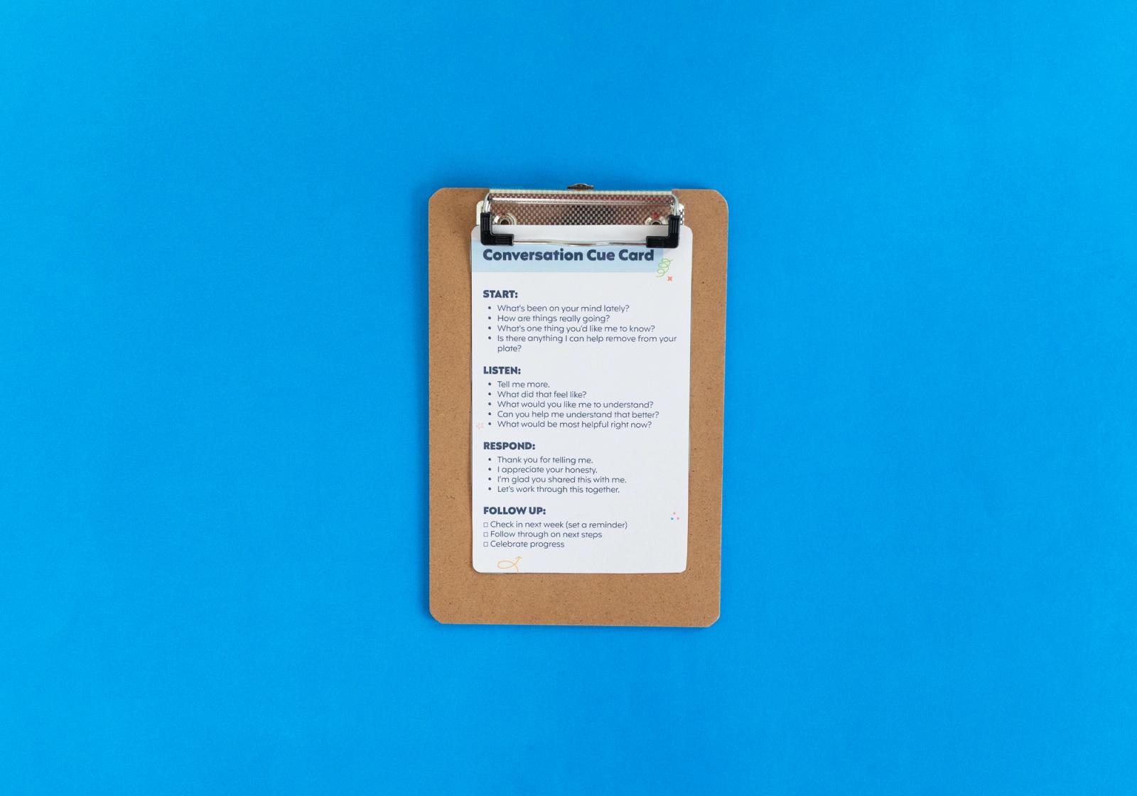 Clipboard with a sheet of paper that says "conversation cue card" lays on a blue background.