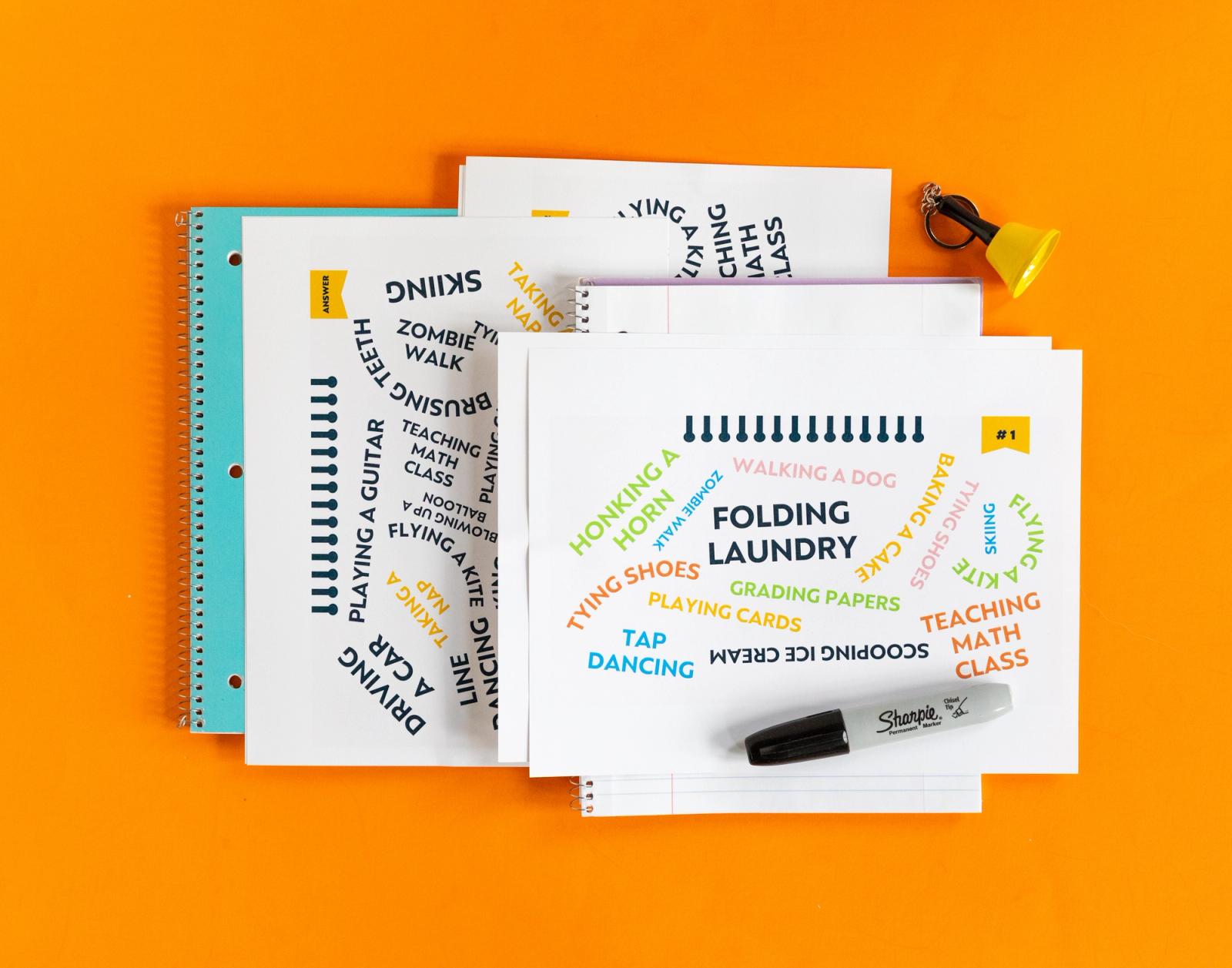 Several pieces of paper, marker, and blue notebook lay on an orange background.