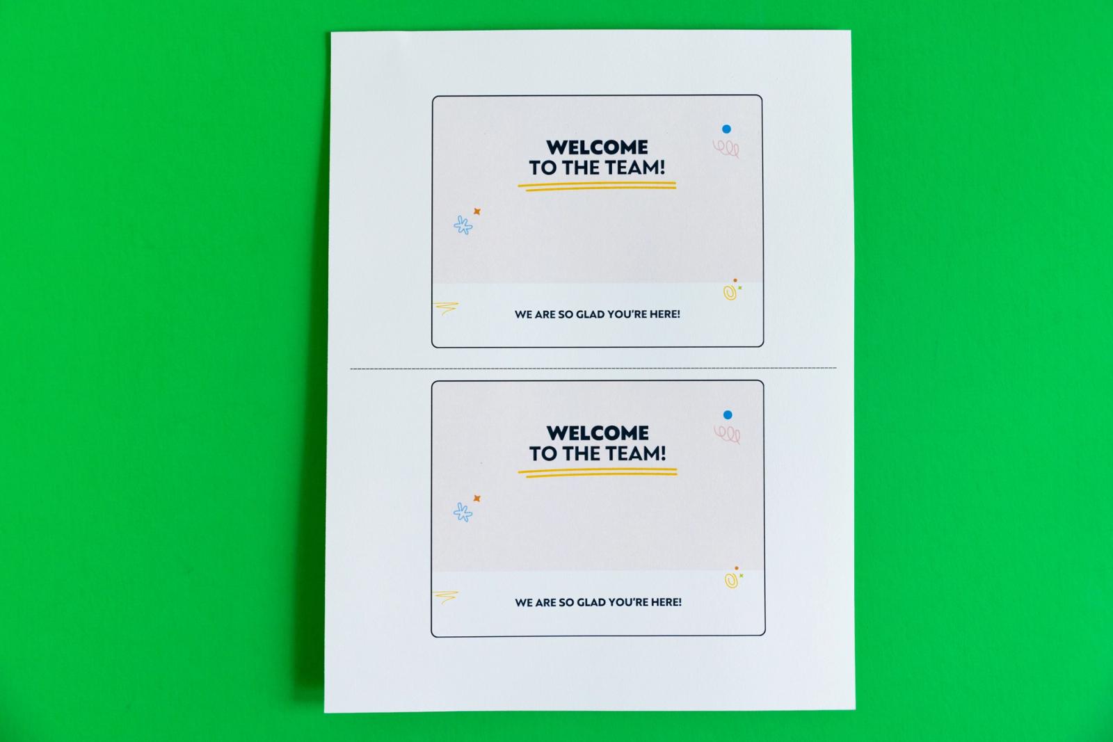 Sheet of paper with two postcards that say "welcome to the team" lay on a green background.