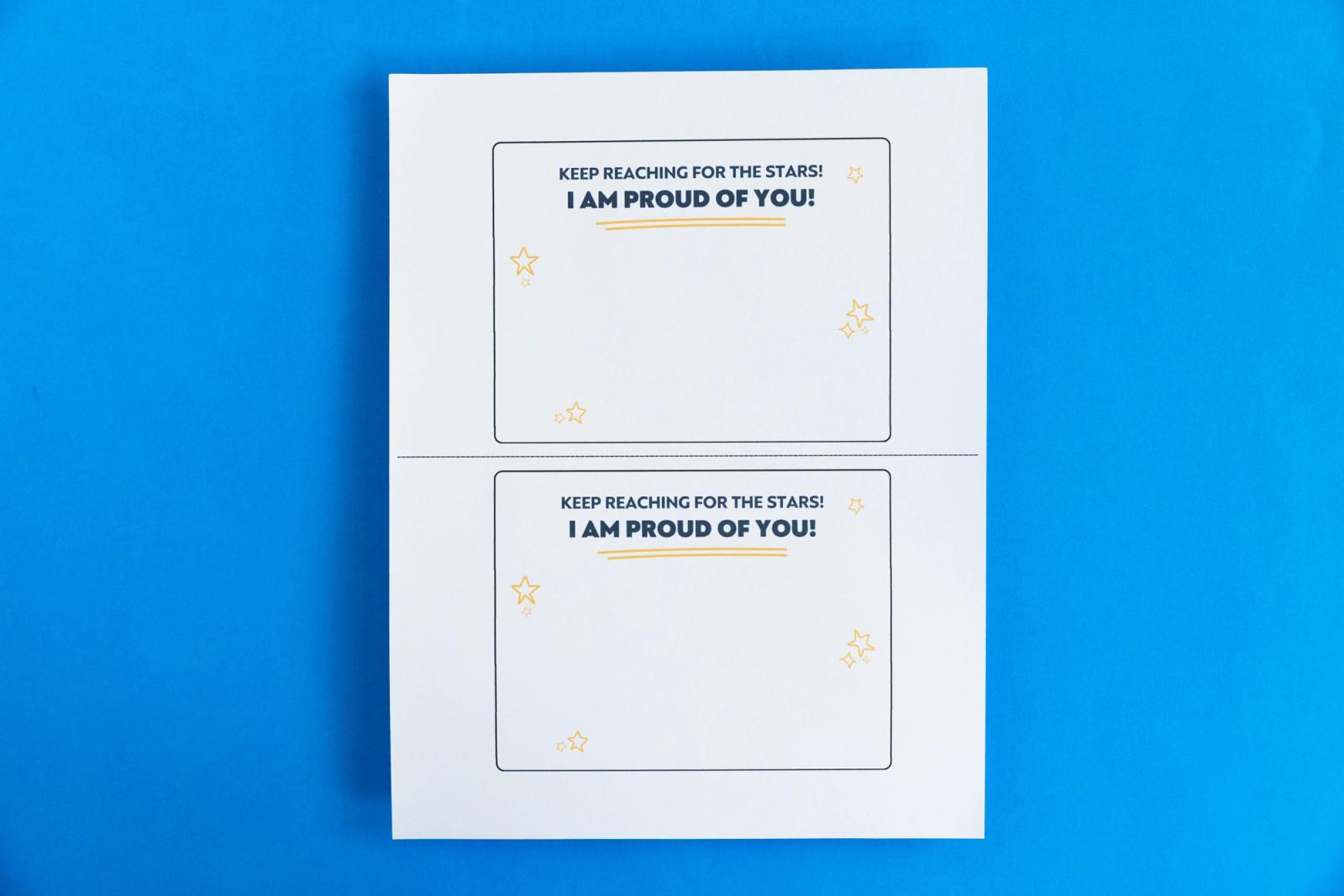 A piece of paper that has two notecards on it that say "I am proud of you" lay on a blue background.