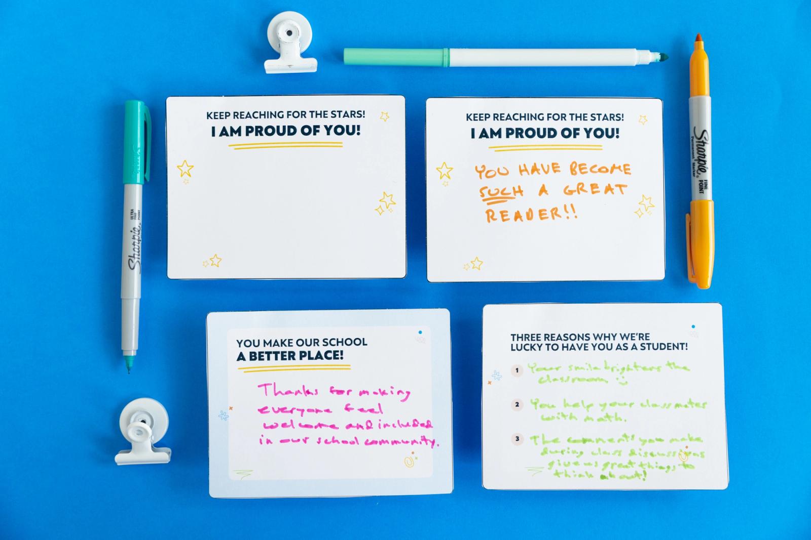 Four notecards lay on a blue background with notes written on them. Markers and paper clips lay around them.