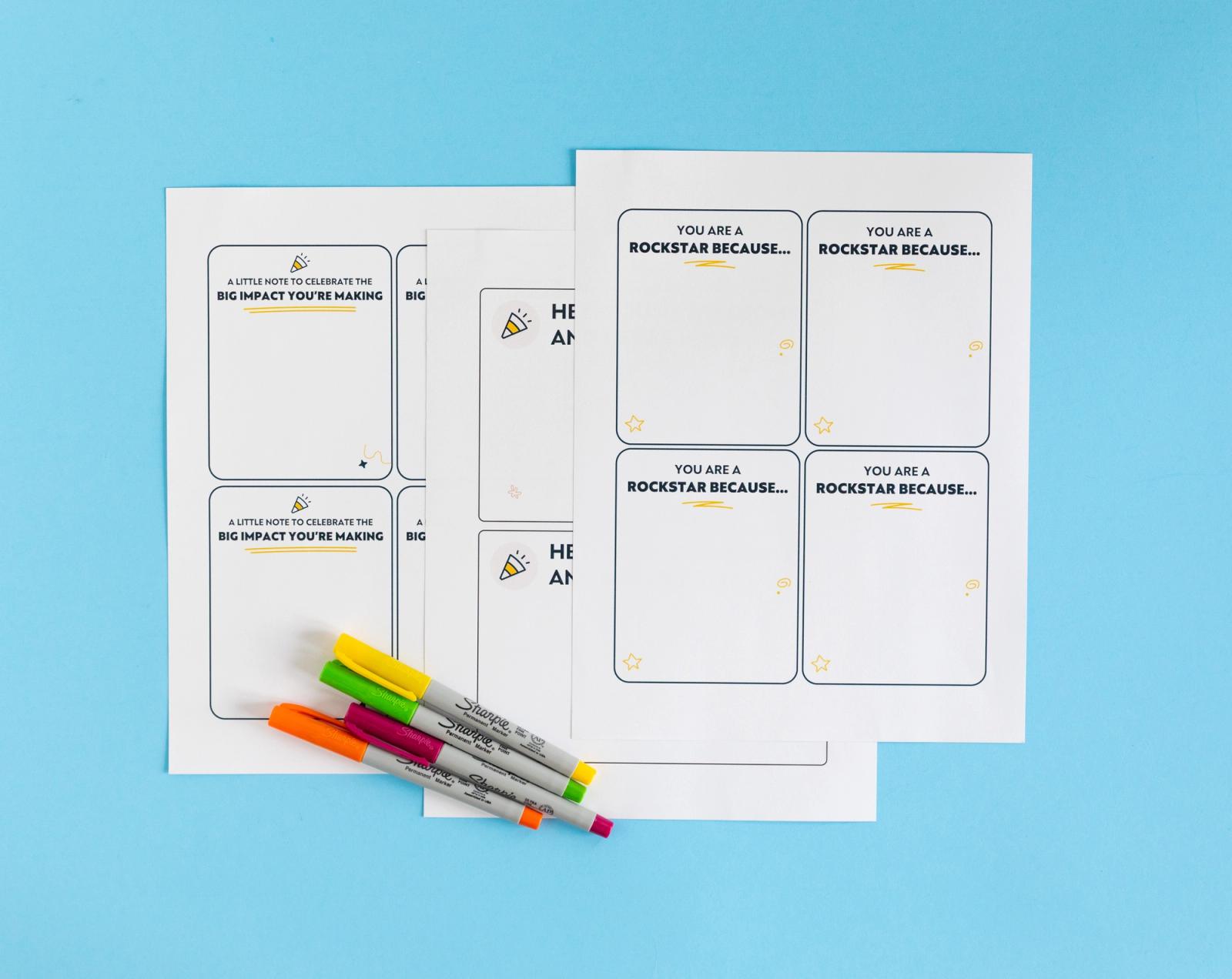 Three sheets of paper with notecards on them lay on a light blue background with colorful pens next to them.