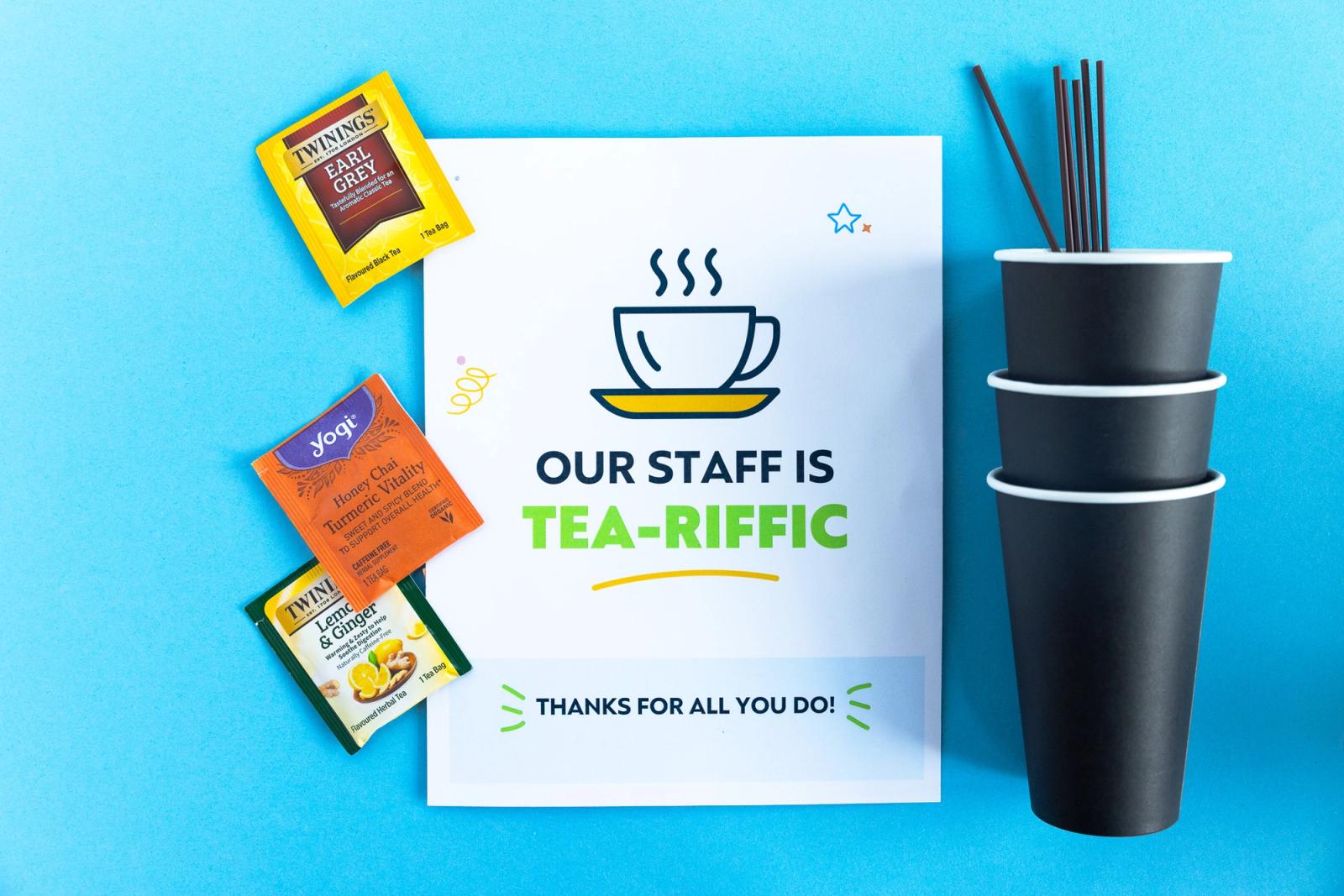 A paper that says "our staff is tea-riffic" lays on a light blue background. To-go cups and tea bags lay around it.