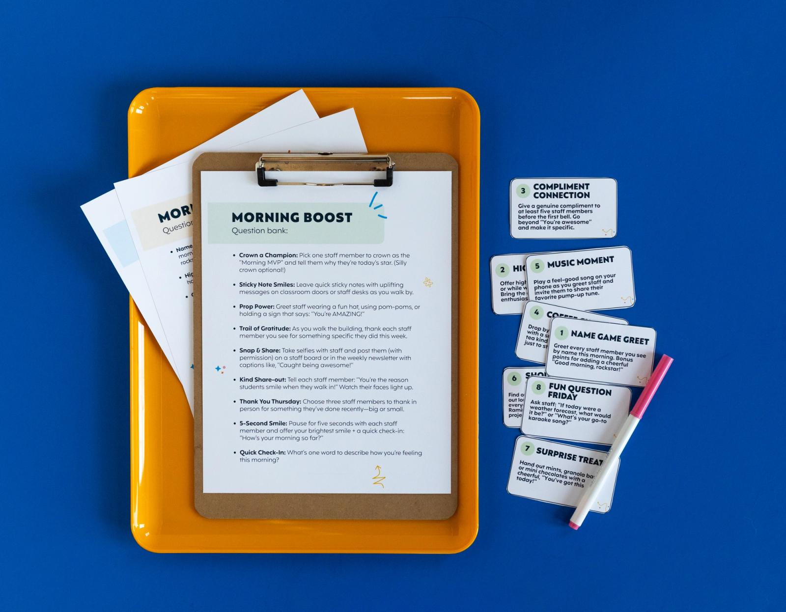 An orange tray lays on a blue background. In it are sheets of paper and a clipboard. Beside it are notecards and a pink marker.