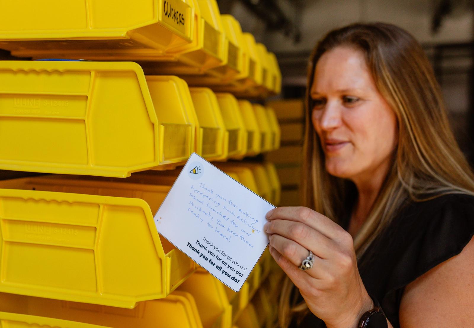 A woman stands in front of a wall of yellow mailboxes and places a postcard in one. 