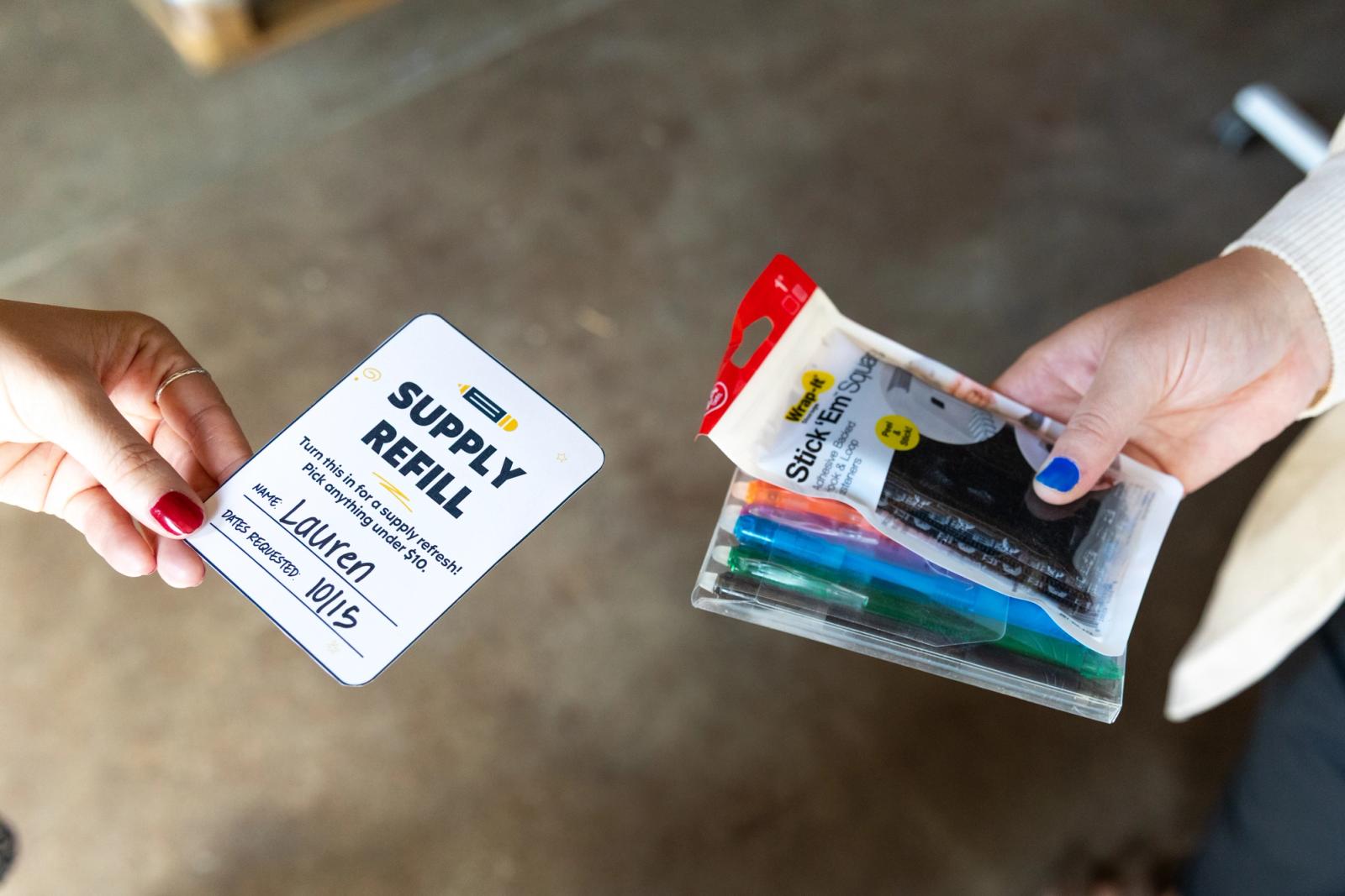 A hand holding a small paper coupon reaches in from the left. A hand holding a package of pens and stickers reaches in from the right.