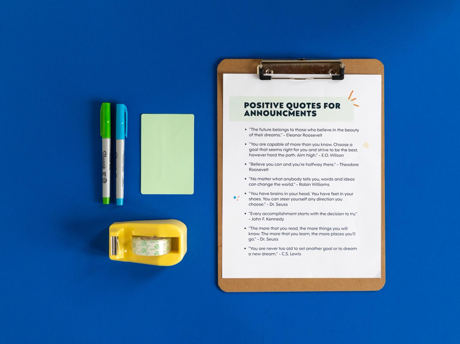 A piece of paper on a clipboard sits on a dark blue background. Beside the clipboard is a yello tape dispenser, green stick notes, and green and blue pens.