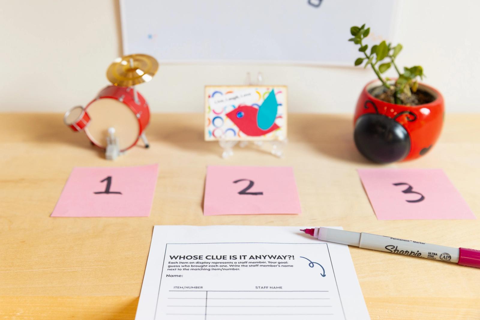 Three small knick knacks sit on a table. A sheet of paper and pen lay in front of them.