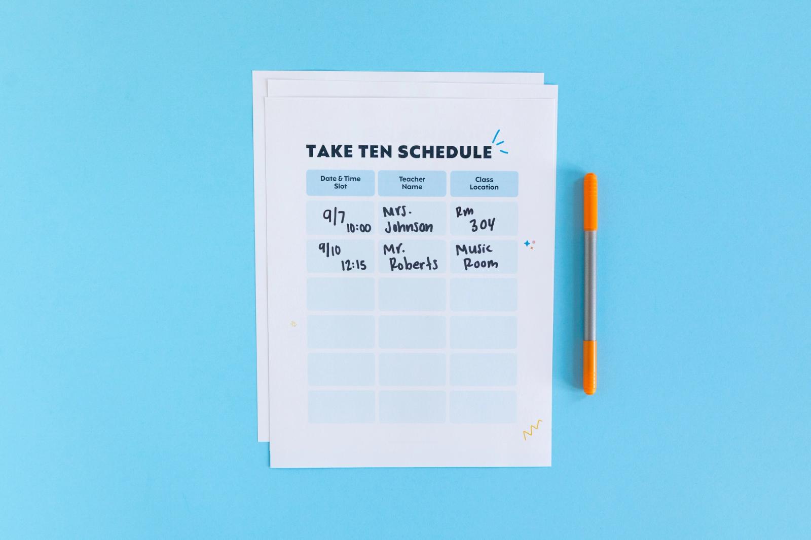 A piece of paper with a schedule on it lays on a light blue background. Next to it is an orange pen.