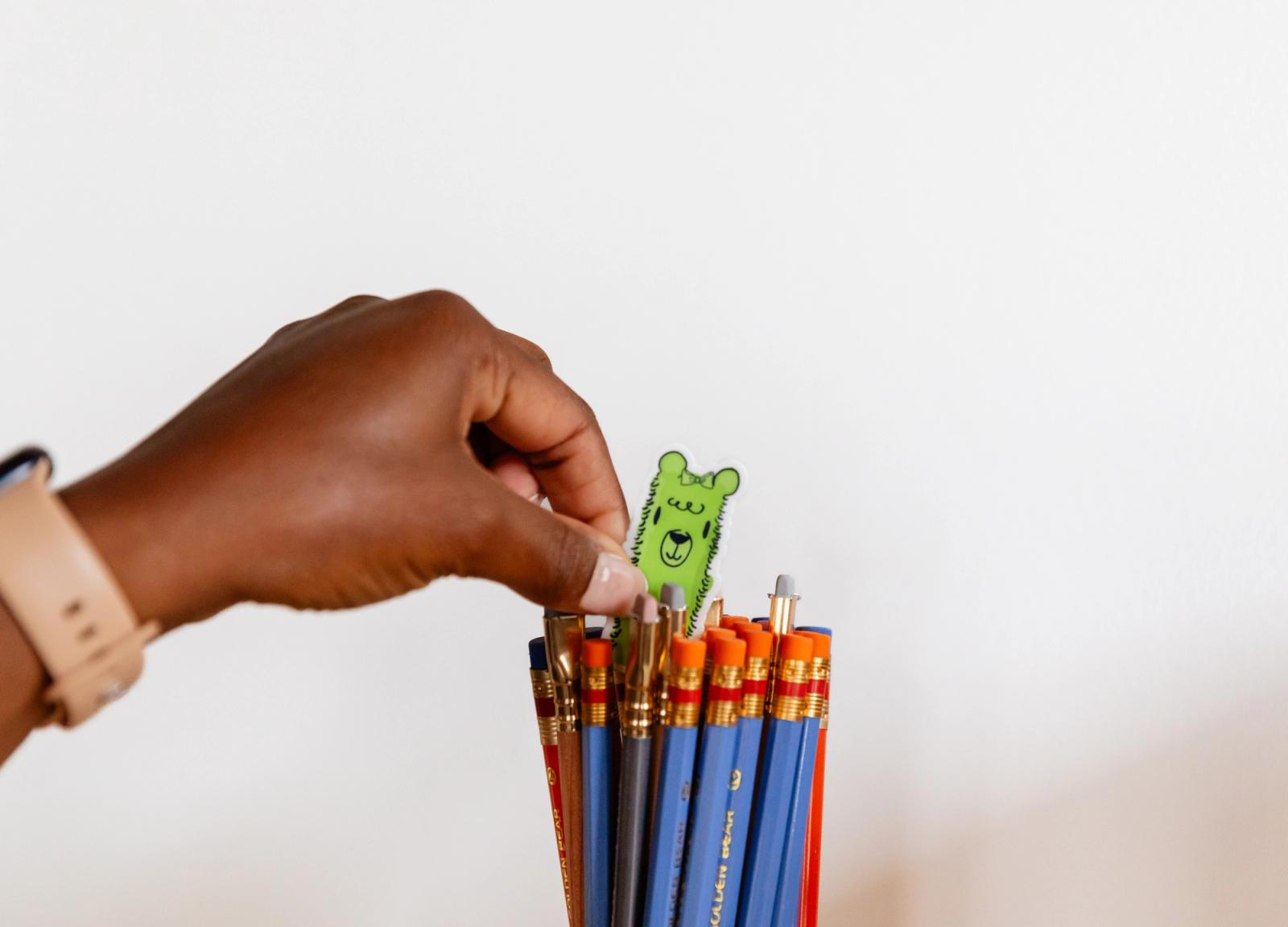 A hand places a small alpaca sticker in a jar of pencils.