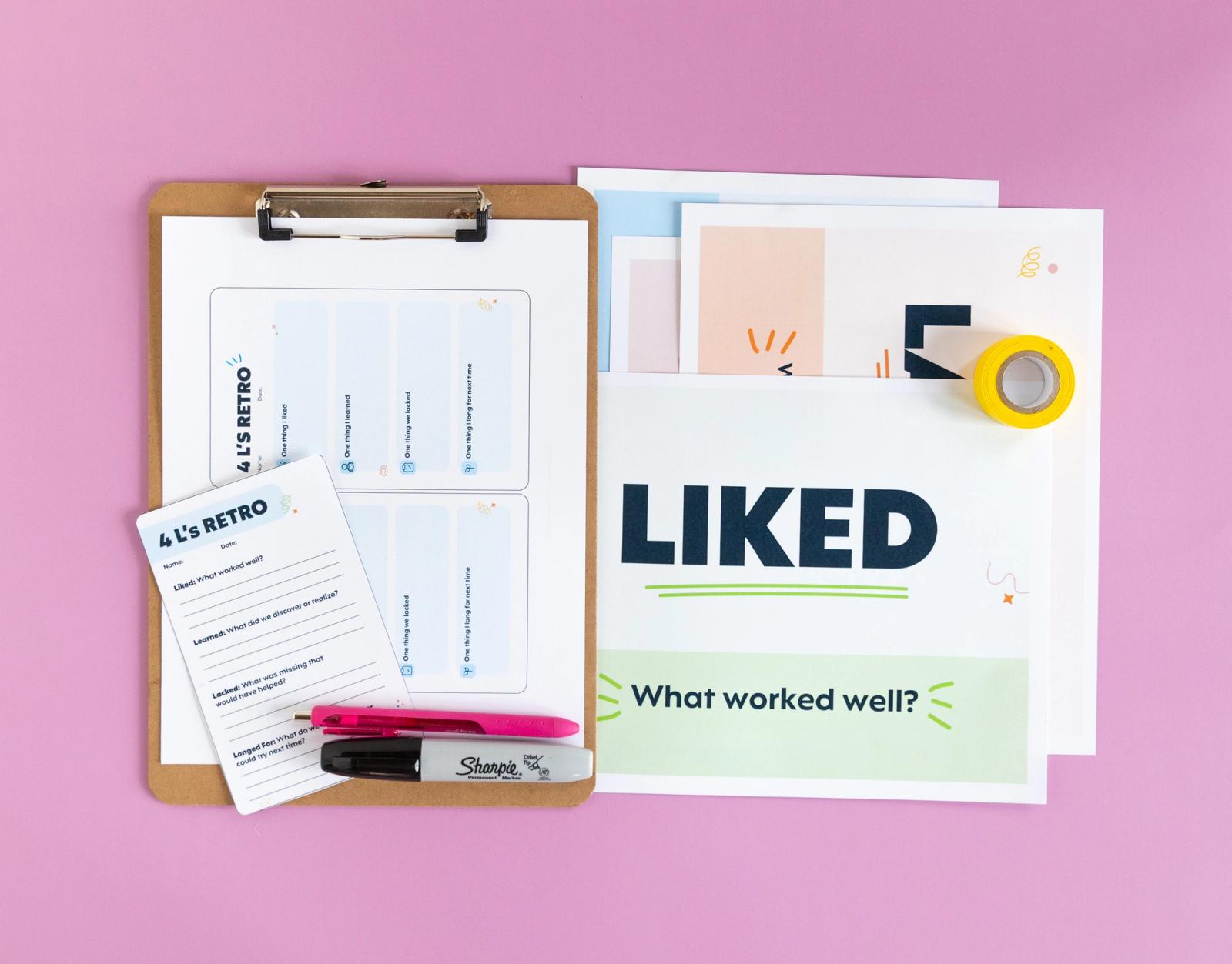 A clipboard with a paper clipped to it and a notcard and pens on top lay on a pink background. Next to it is a piece of paper that says "liked."