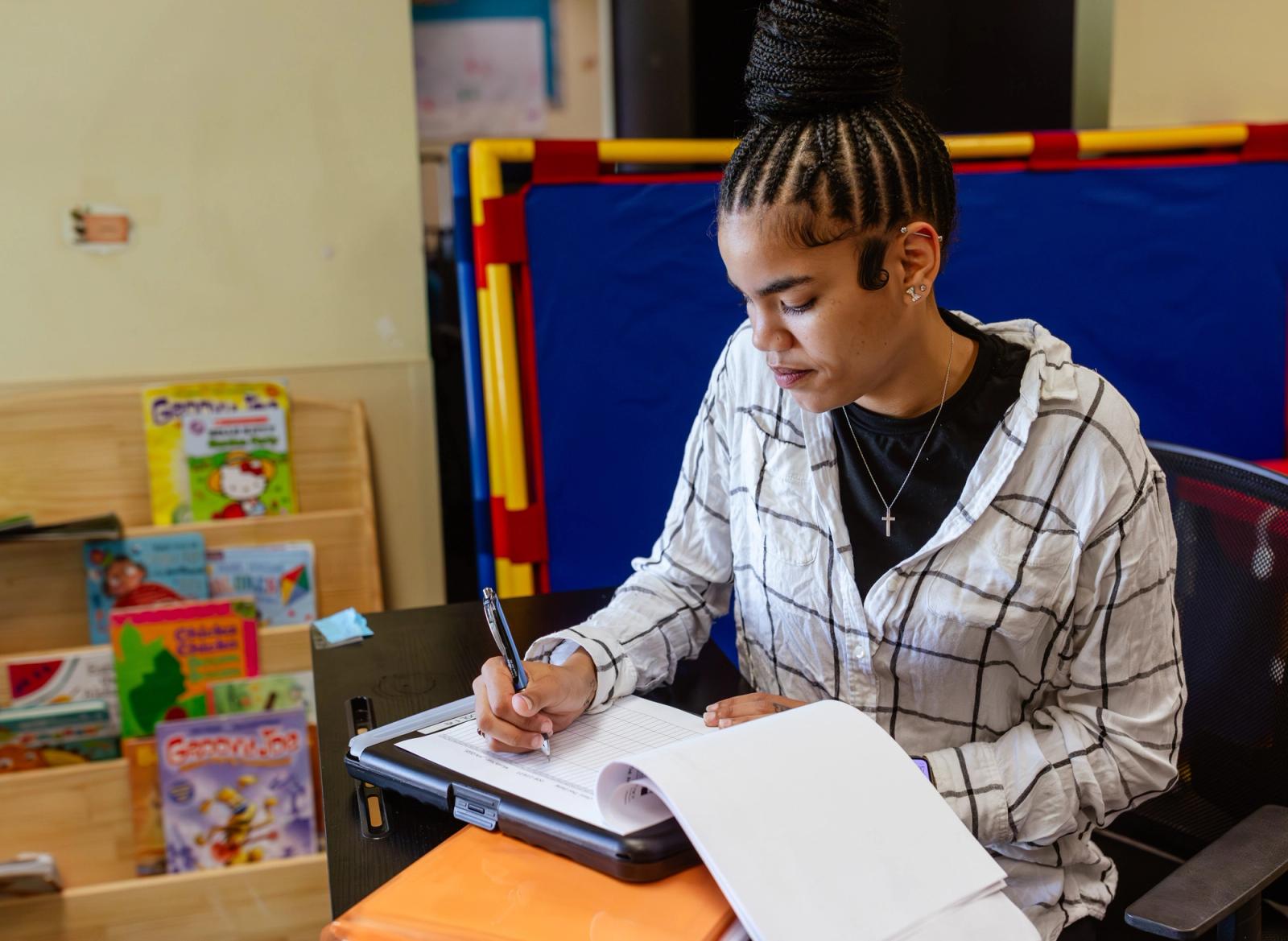 A women sits in a classroom at a desk grading papers.