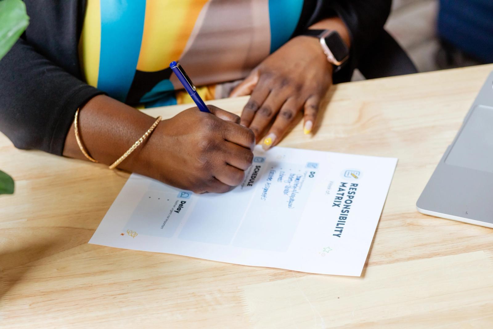 A woman sits at a wooden desk writing on a piece of paper.