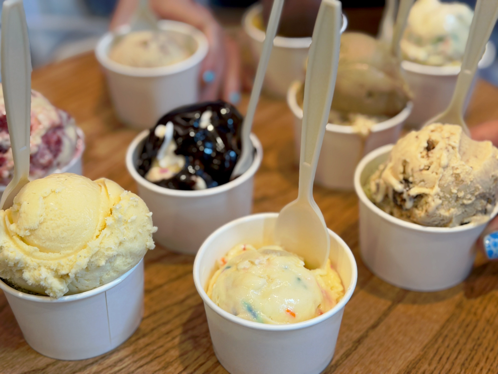 Small dishes of ice cream with spoons in them sit on a table.