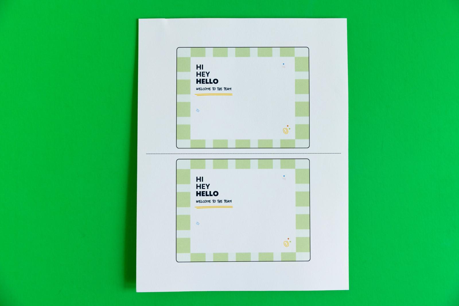 A piece of paper with two postcards that say "hi, hey, hello" on them lays on a green background.