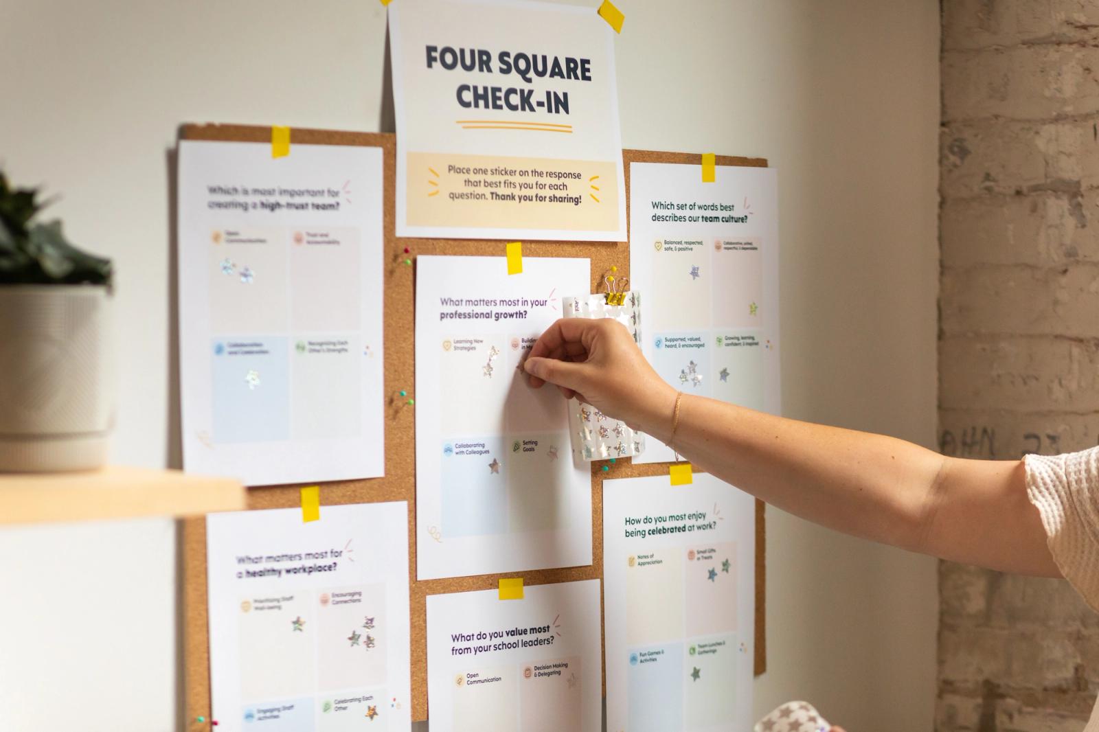 A bulletin board is covered in pieces of paper with gold stars on them. A hand reaches in from the right to place another sticker.