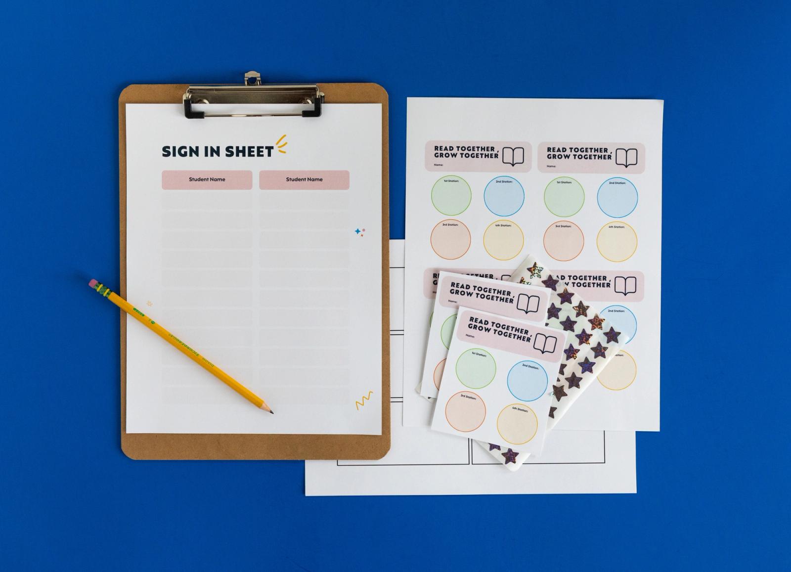A clipboard with a sign-in sheet and a pencil on it lay on a blue background. Sheets of paper and stickers lay next to it. 