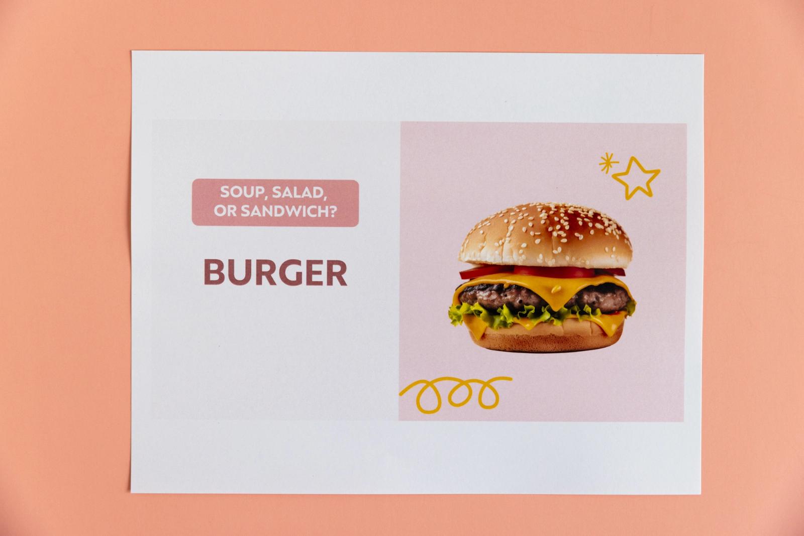 Piece of paper with a picture of a burger and "soup, salad, or sandwich?" lays on a peach background.