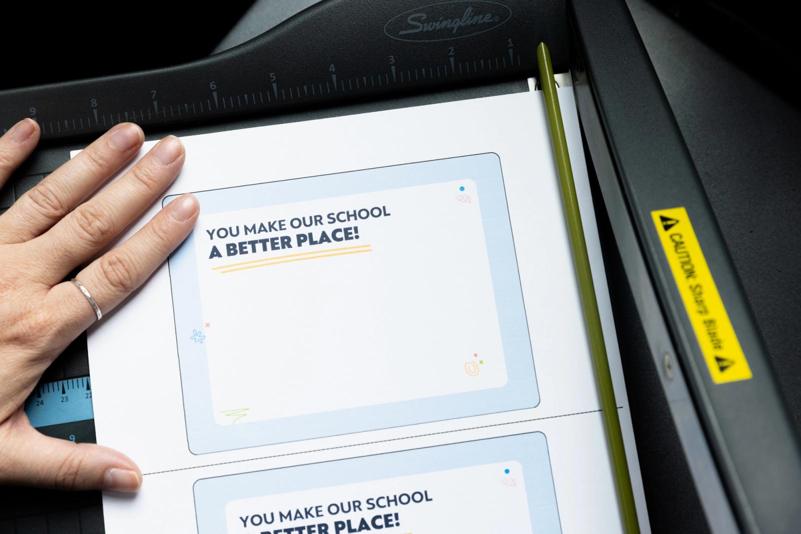 A hand cuts out postcards that say "you make our school a better place."