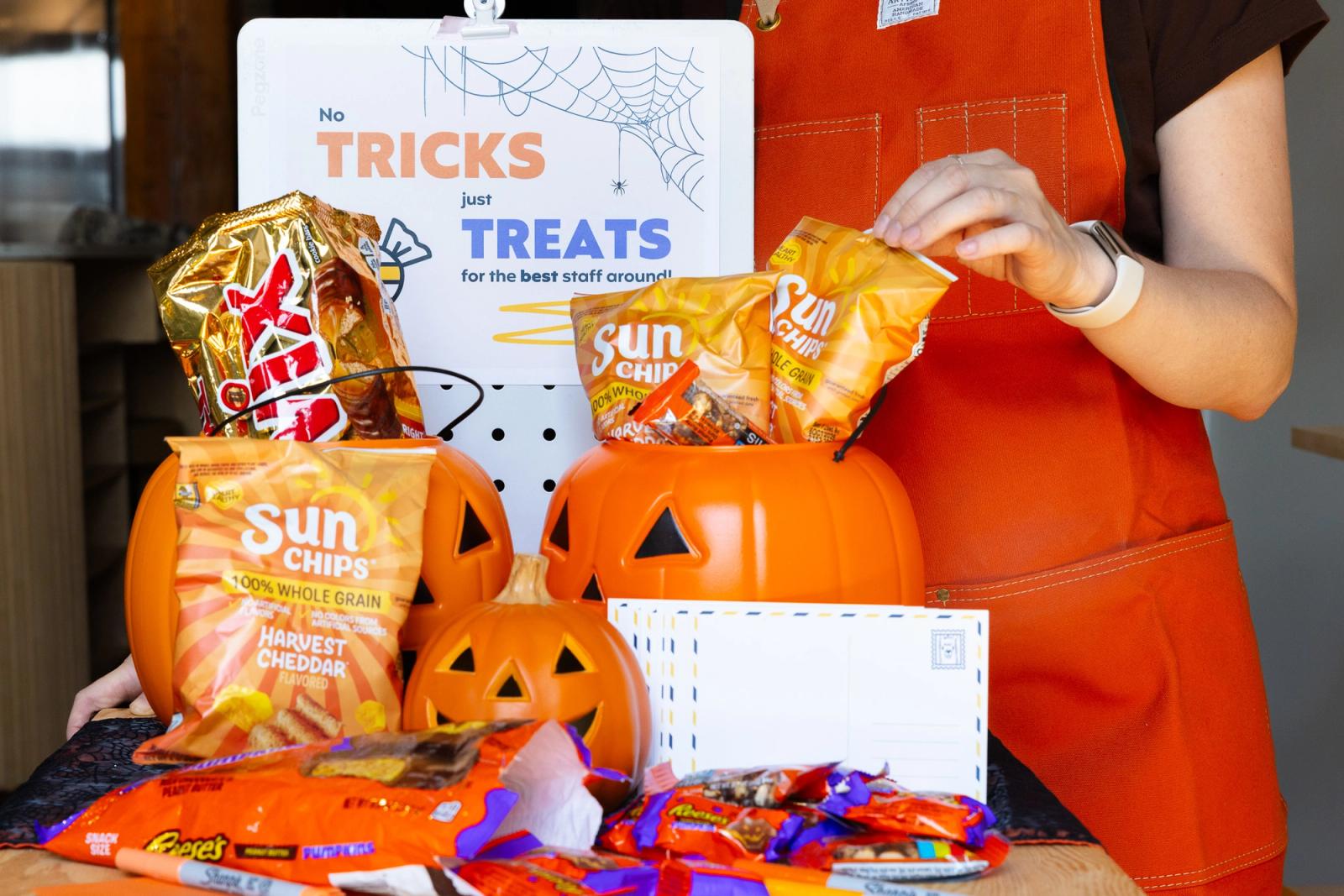 Someone stands in front of a cart with pumpkins and orange treats on it.