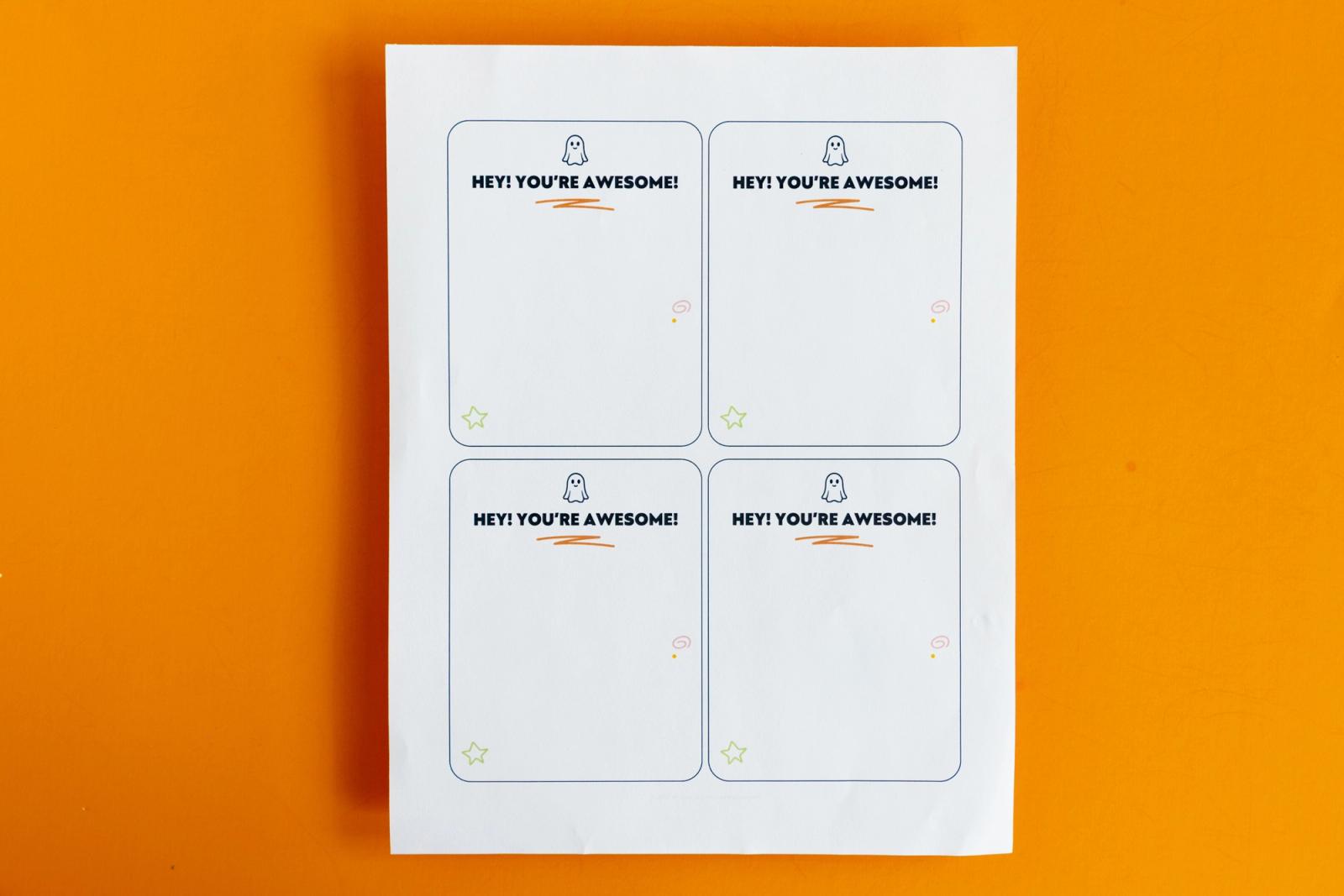 A piece of paper with four notecards that say "hey! you're awesome" lays on an orange background.