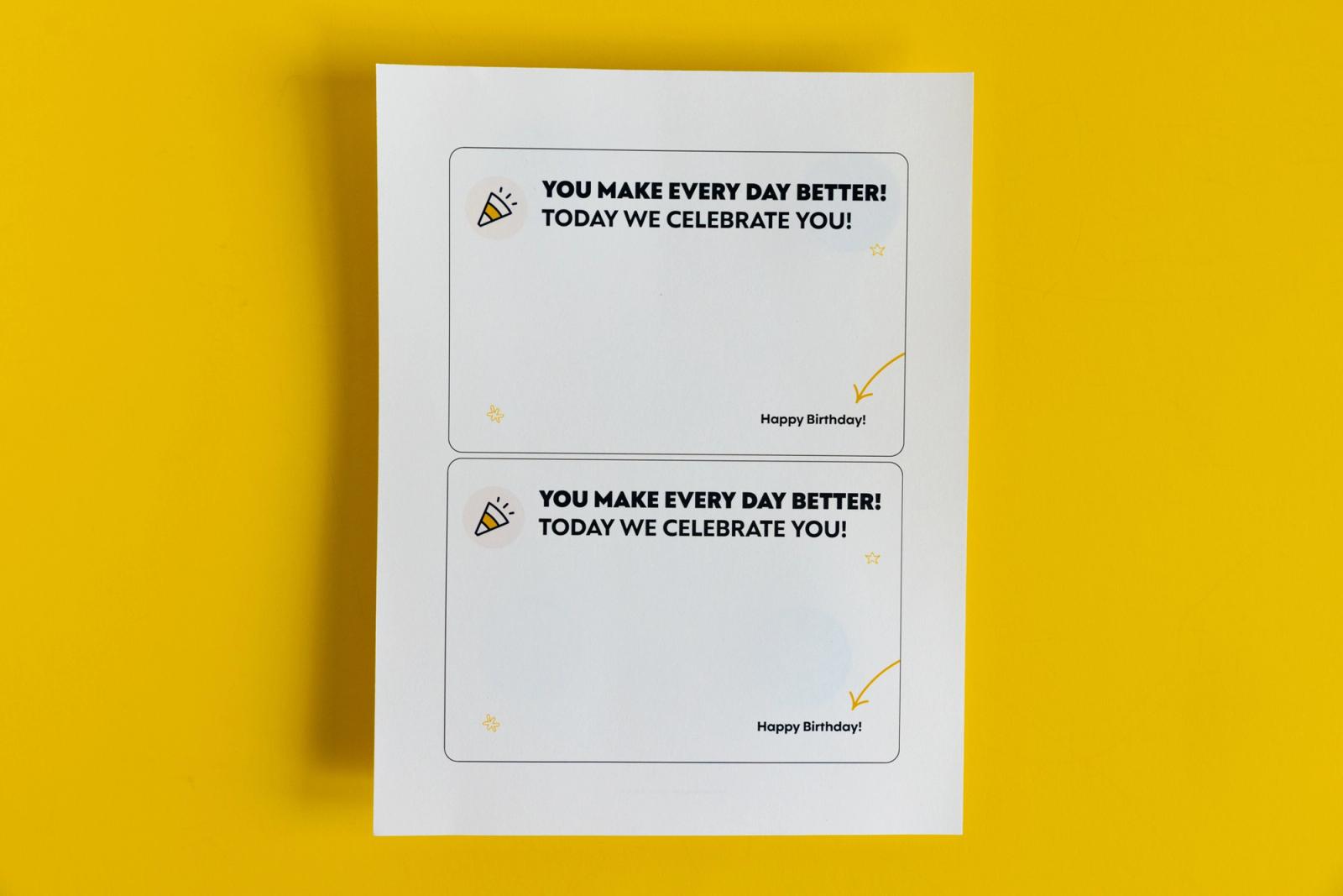 A piece of paper with two notecards that say "you make every day better! today we celebrate you!" lay on a yellow background.