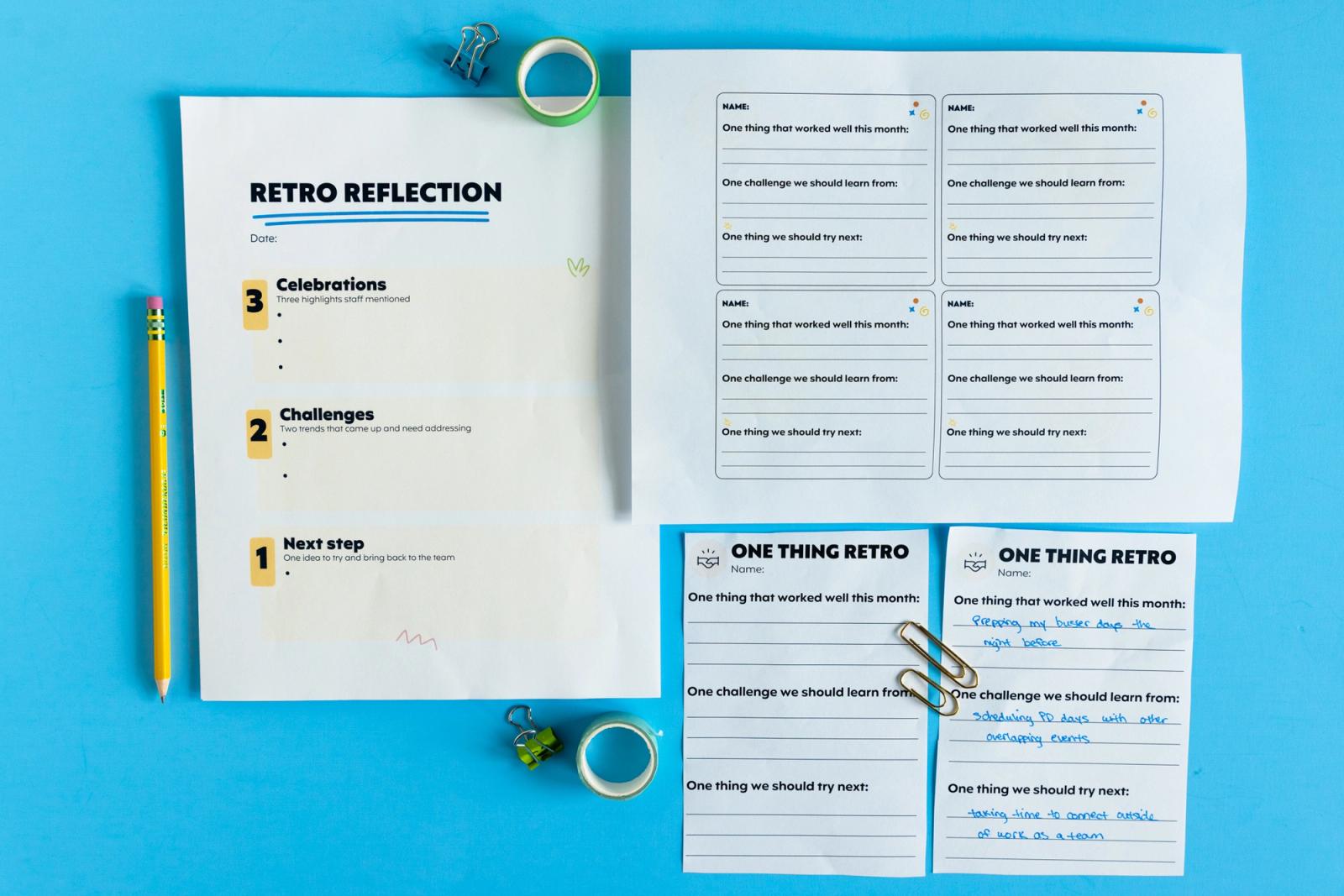 Sheets of paper lay on a light blue background. Pencils, tape, and paper clips lay around them.