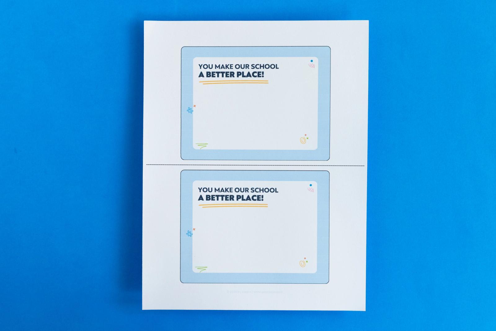 A piece of paper that has two notecards on it that say "you make our school a better place" lay on a blue background.