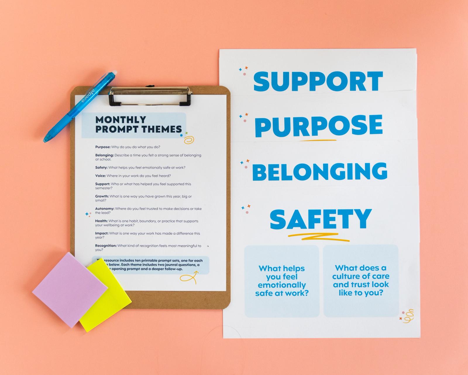 A sheet of paper on a clipboard sits on alight orange background. A blue pen and sticky notes sit on the clipboard. Beside it are posters the words support, purpose, belonging, and safety on them.