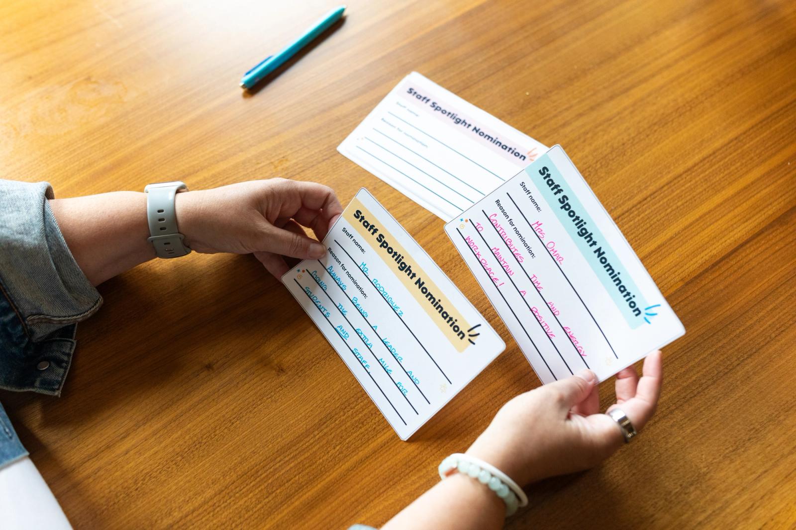 A woman sits as a wooden table and shuffles through several staff spotlight nomination cards.