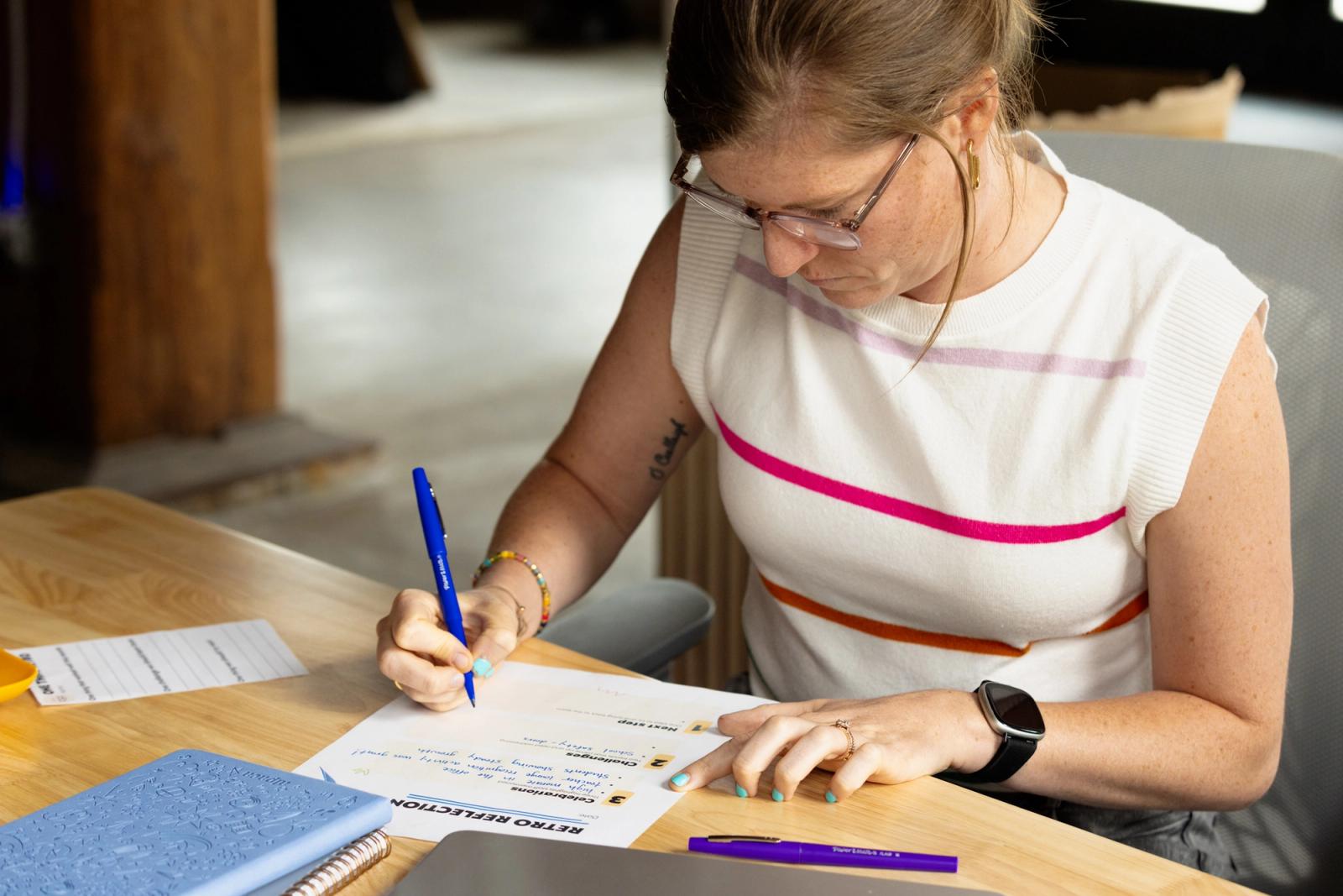 A woman sits at a desk and writes on a piece of paper.