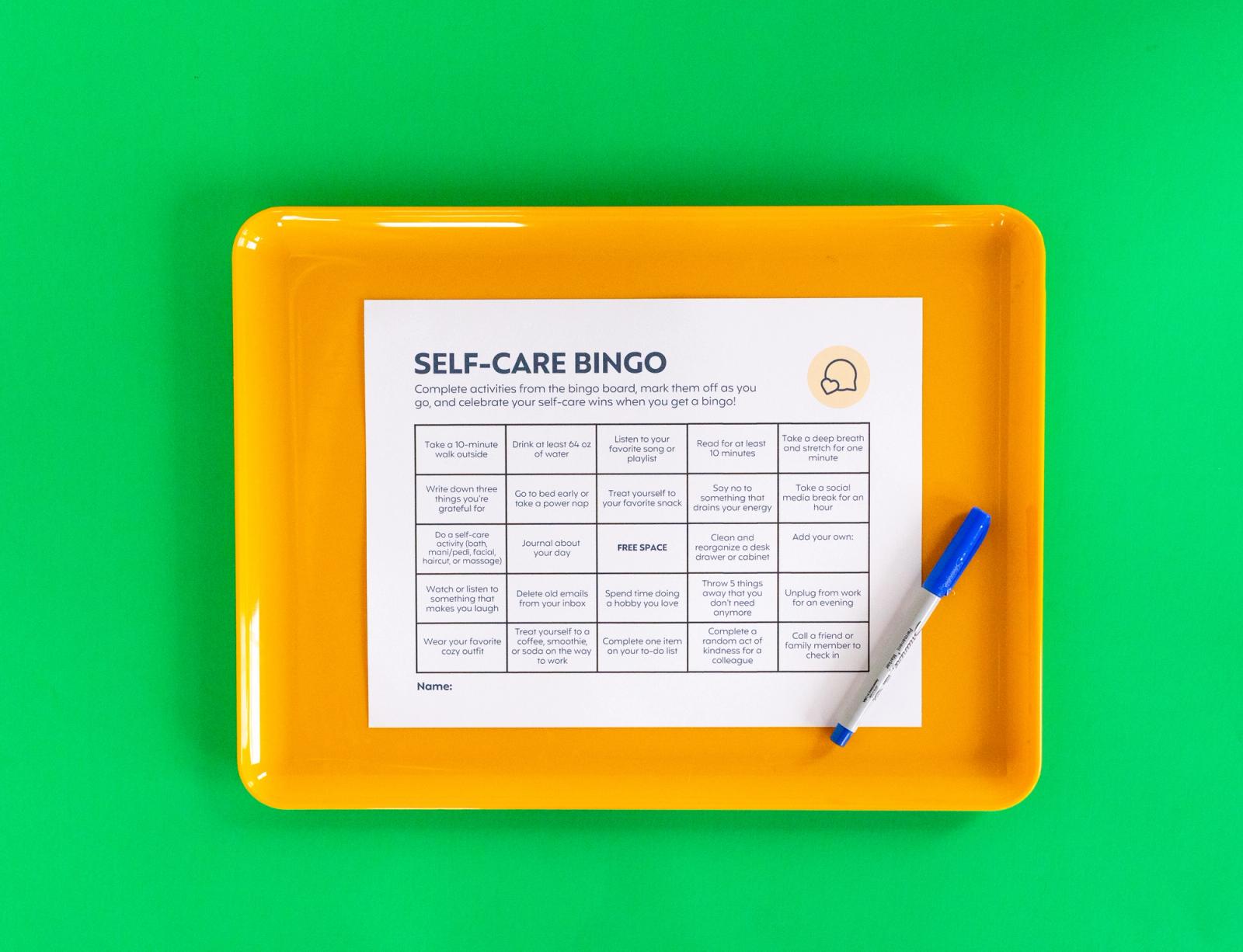 A sheet of paper and blue pen lay on an orange tray on a green background.