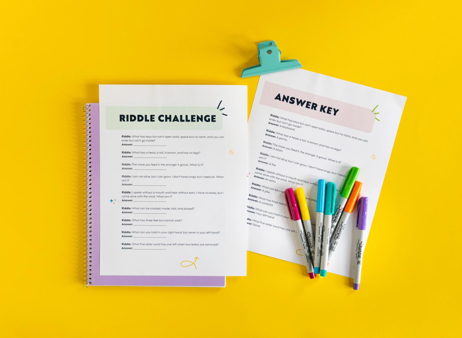 Two sheets of paper, a purple notebook, and markers lay on a yellow background.