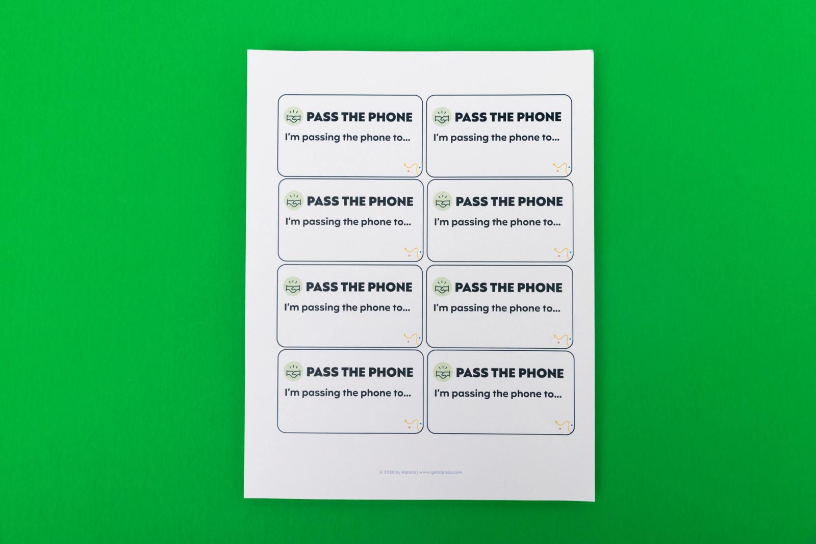 A sheet of paper with small notecards that say "pass the phone" on them lays on a green background.