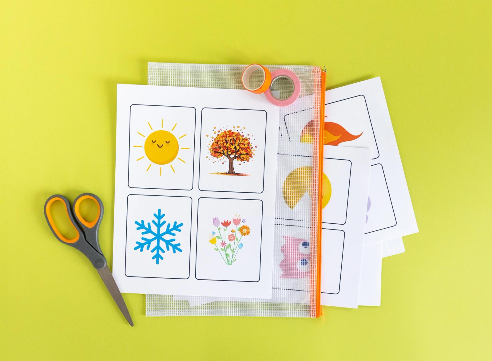 A sheet of paper with four images representing the seasons lays on top of a clear bag with more papers in it on a yellow background. A roll of tape and pair of scissors lay next to it. 