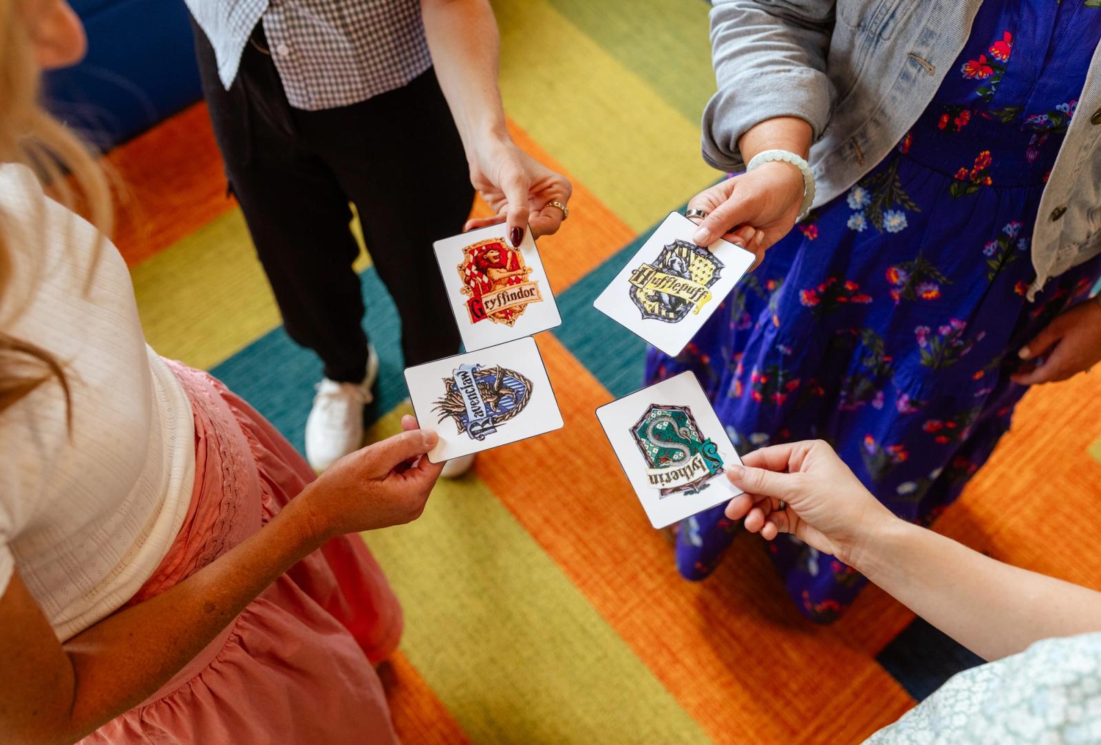 Four people stand in a circle with a colorful rug in the background. They each hold a small piece of paper with an image on it and the images meet in the middle of the circle.